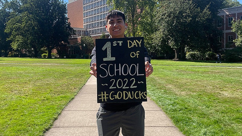A student poses with a sign for the first day of classes