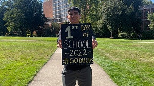 A student poses with a sign for the first day of classes